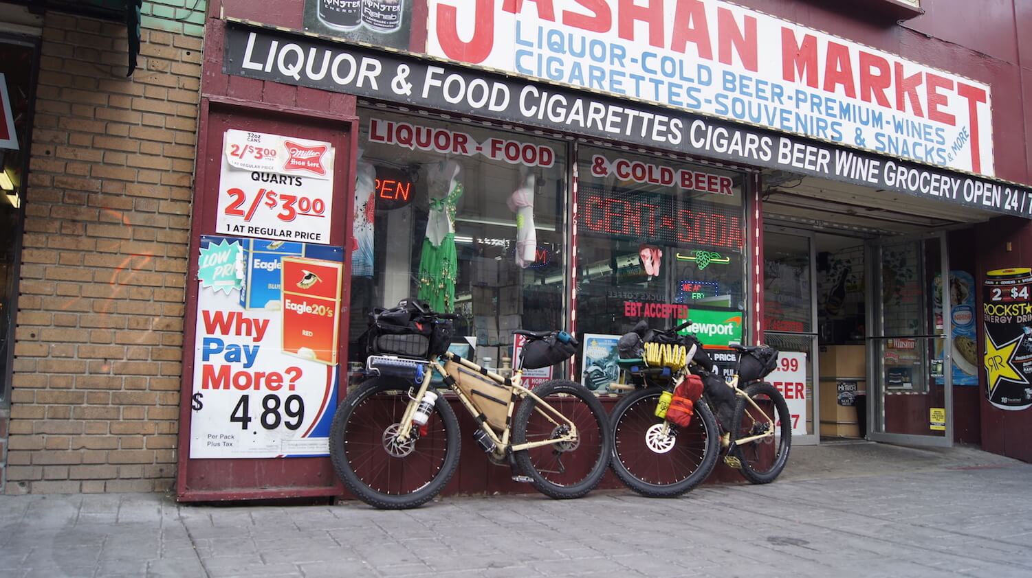 Left side view of 2 Surly fat bikes, loaded with gear, in front of a market
