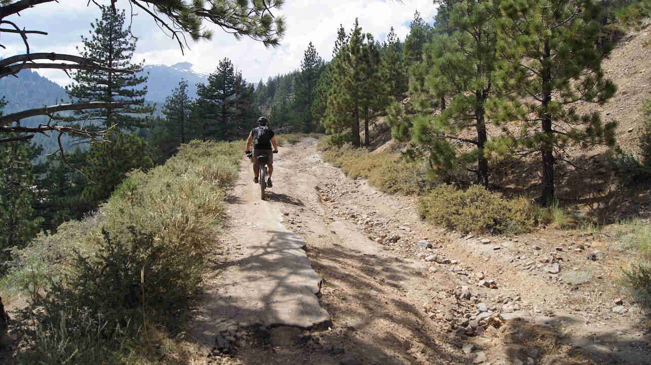 Rear view of a cyclist riding up the hill of a rocky trail in the mountains
