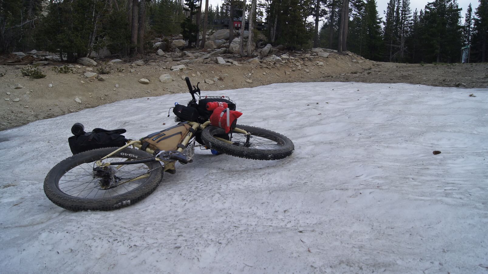 A Surly bike, loaded with gear, laying on a large sheet of ice, in a clearing in the forest