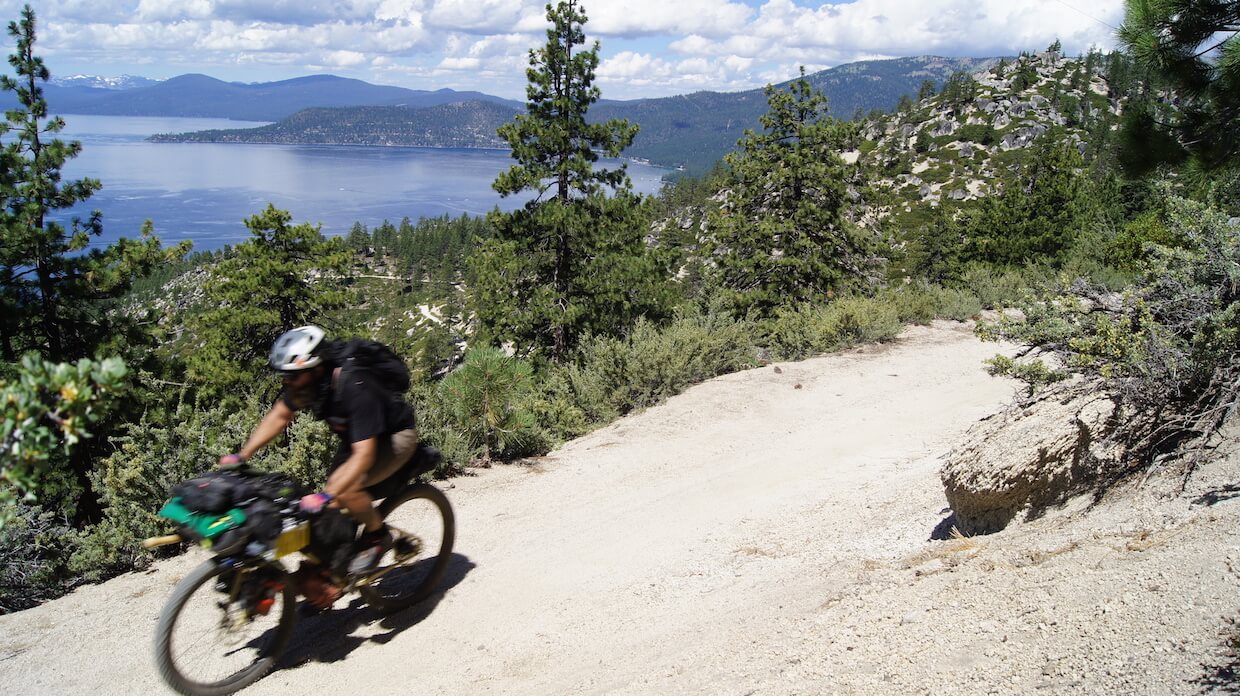 Downward view of a cyclist on a gravel mountain trail, with a lake below in the background