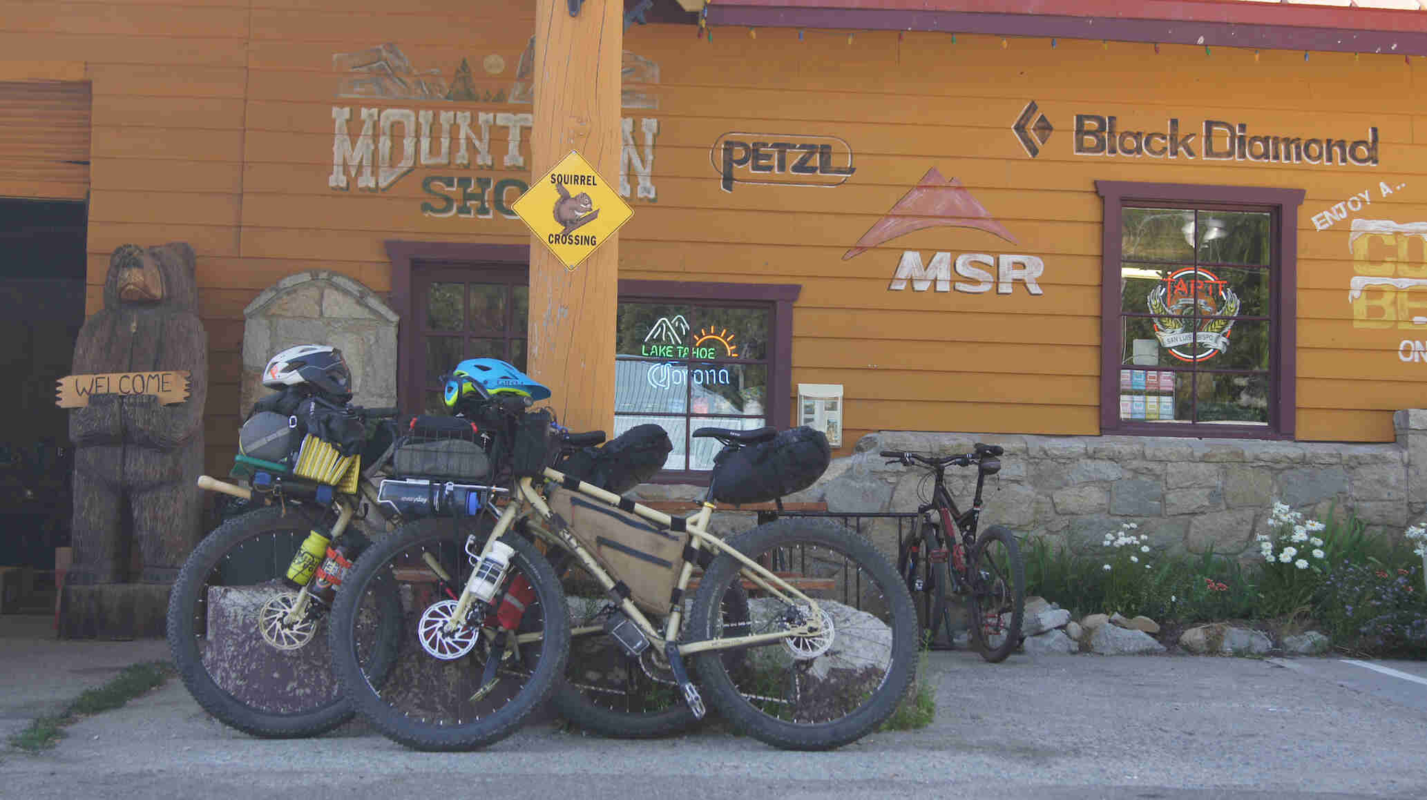 Left profile view of 2 Surly fat bikes, loaded with gear, side by side in front of an orange Mountain Shop building