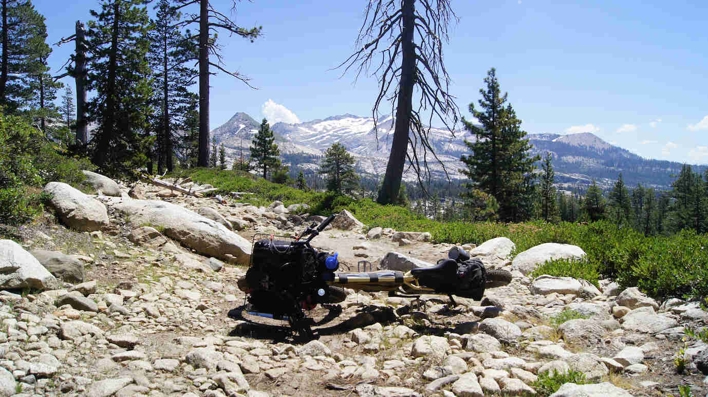 A Surly bike laying on top of rocks, with trees and mountains in the background