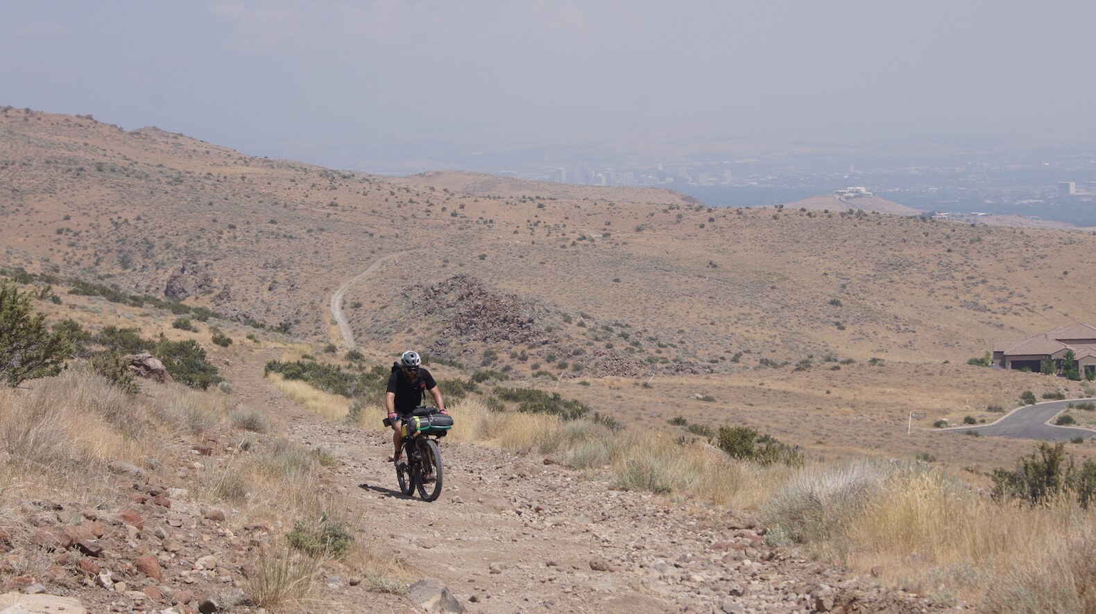 Front view of a cyclist riding up a hill of a gravel trail, with mountain hills in the background