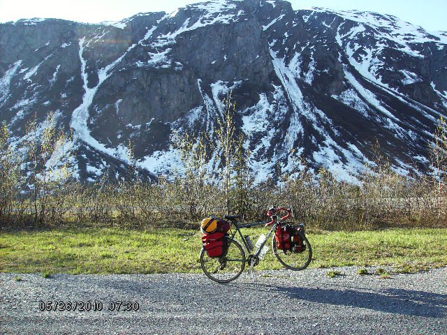 Right side view of a Surly bike with saddlebags, on the side of a gravel road, with snowy mountains in the background