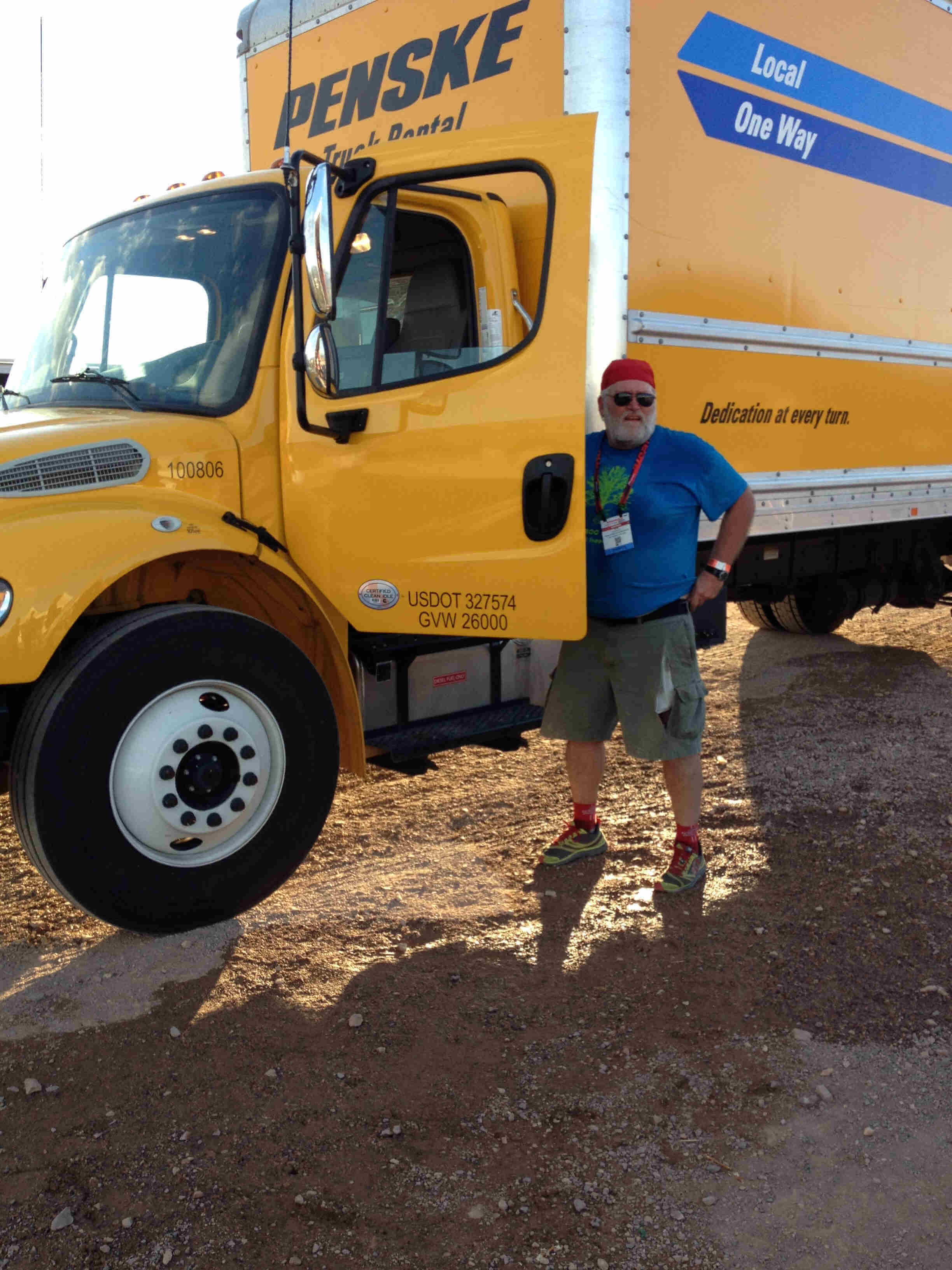 A person standing next to an open door on the left side of a yellow Penske moving truck