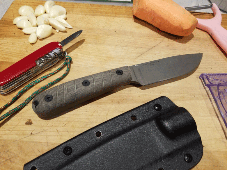 Garlic cloves, sweet potato, potato peeler, swiss army knife, gray fixed blade knife and a sheath on wood cutting board