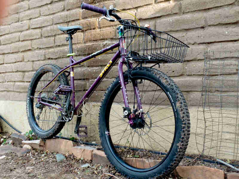 Right side view of a purple Surly bike, parked against a brick wall