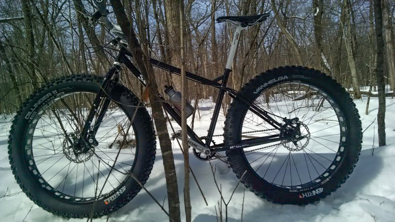 Left side view of a black Surly Pugsley fat bike, parked on deep snow in the woods