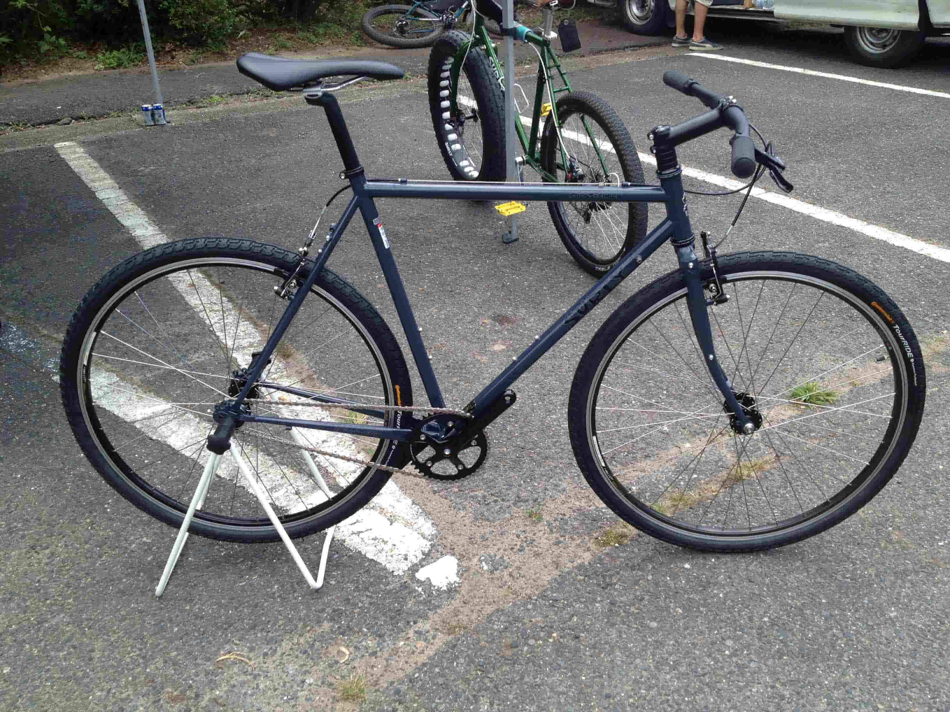 Right side view of a dark blue Surly Cross Check bike, standing across a paved parking lot spot, with a bike behind it