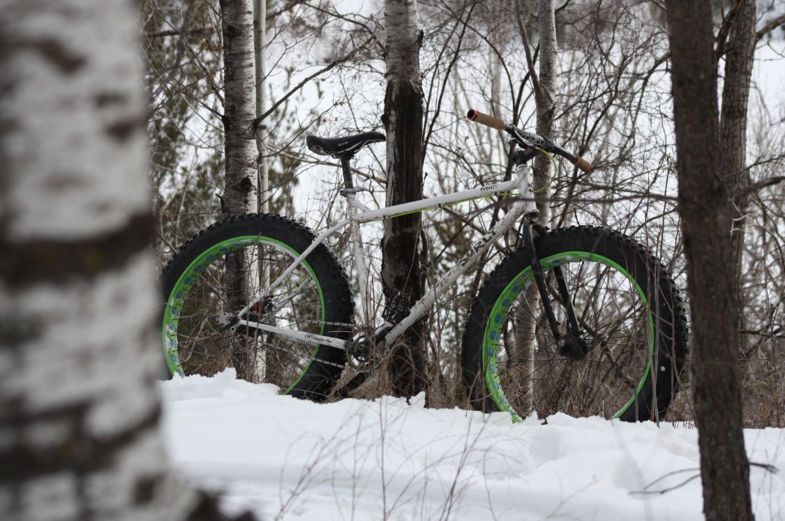 Right side view of a white Surly Pugsley fat bike, parked on snow in the woods