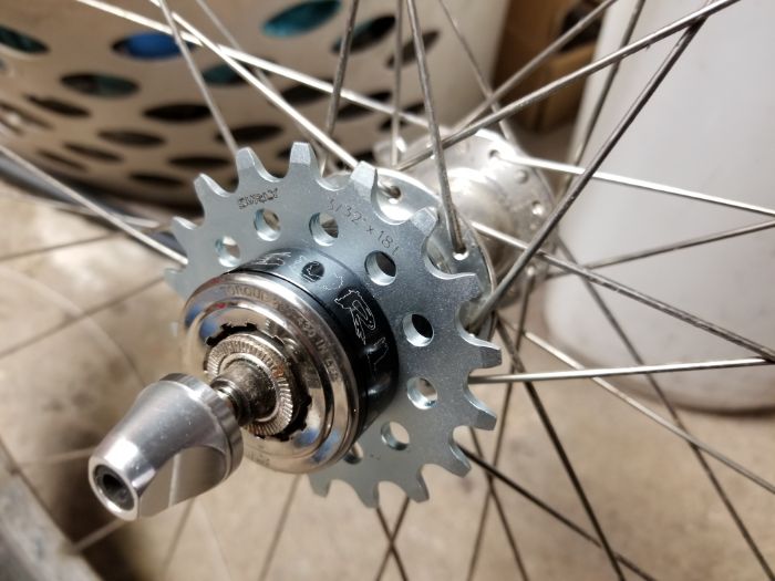 Zoom in view of a Surly bike gear mounted on a  hub with spokes with a laundry on a concrete floor showing in background