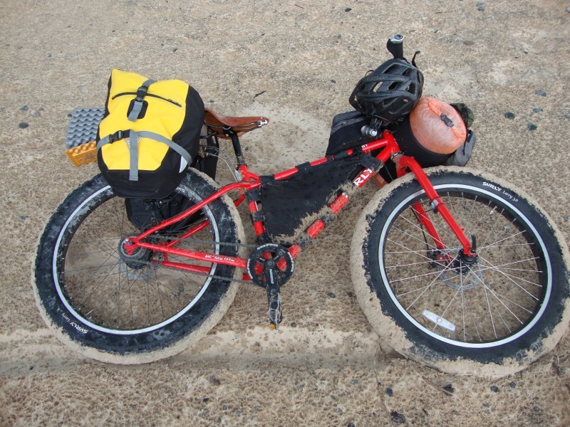 Downward, right side view of a red Surly Pugsley fat bike, loaded with gear, laying on it's side in wet sand