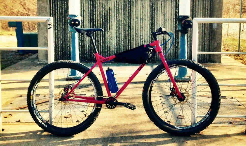 Right side view of a Surly 1x1 teaberry bike, parked along a split handrail on a cement platform 