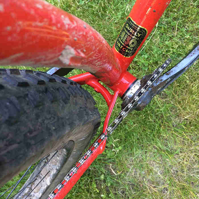 Downward close up view of a cranks and chainstay plate on a Surly Krampus bike, red, with green grass below