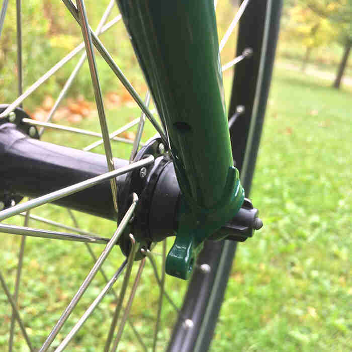 Zoomed in view of the lower fork and front hub on a green Surly Pack Rat bike with grass shown in the background