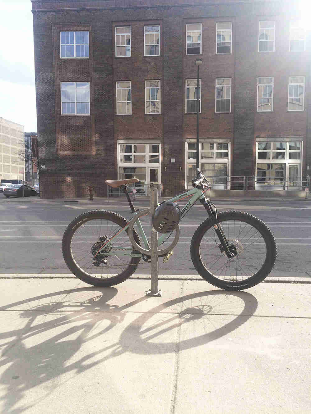Right side view of a Surly Wednesday bike parked on a sidewalk behind a steel post, with a building in background