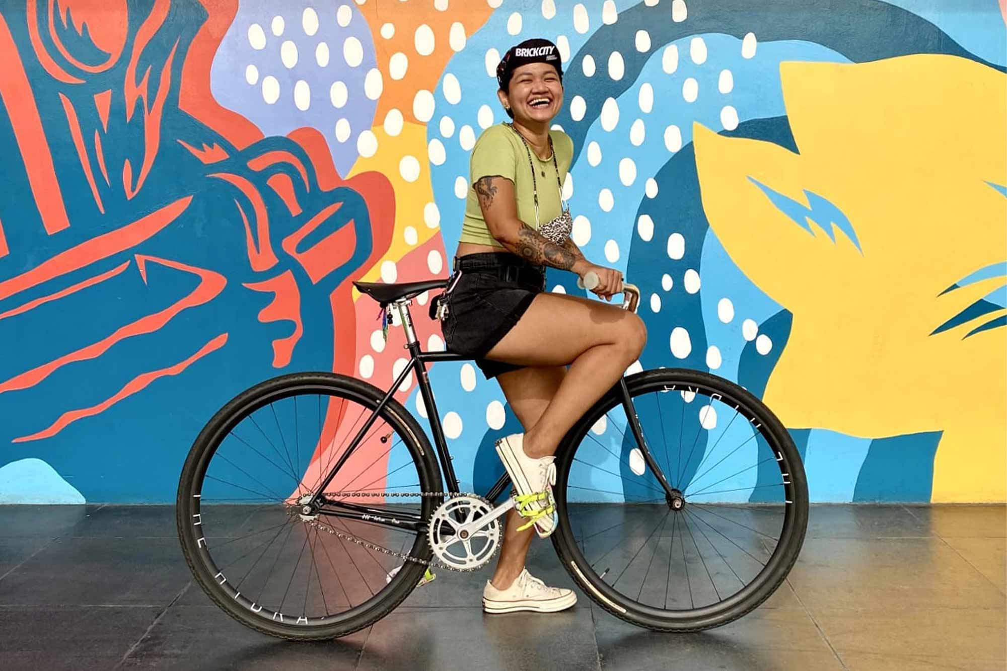 Aneka on Surly Steamroller bike with one foot down, smiling, in front of mural