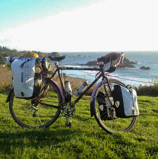 Right side view of a Surly bike, parked in grass, with a shoreline and the ocean in the background
