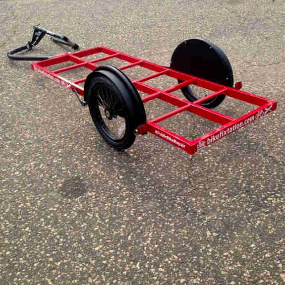 Downward view of a red bike trailer, with black wheels, sitting on pavement