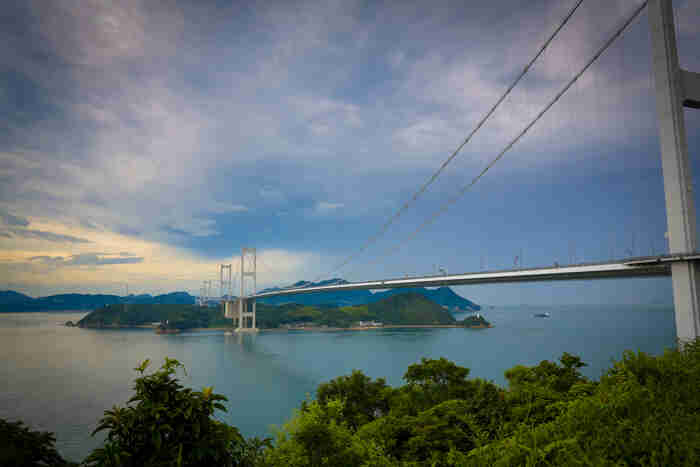 Angled, left side view of a suspension bridge, spanning over a bay on a cloudy day