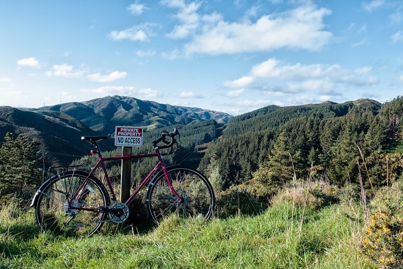 Right side view of a red Surly bike, parked on a grassy hilltop, overlooking a valley of trees and mountains
