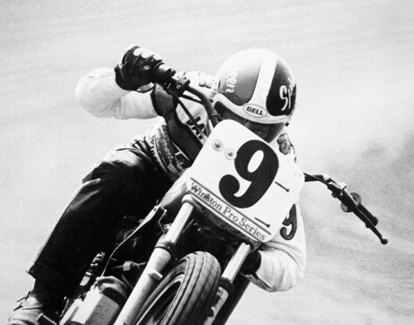 Black & white image - Front view of a motorcycle rider, tucked down behind the race plate, while racing their motorbike