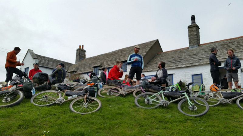 Upward view of cyclists on a grassy hill with their bikes, and a building behind them in the background