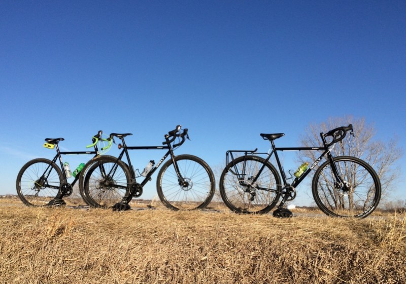 Right side view of three, black Surly Straggler bikes, lined up inline, on a field of brown grass