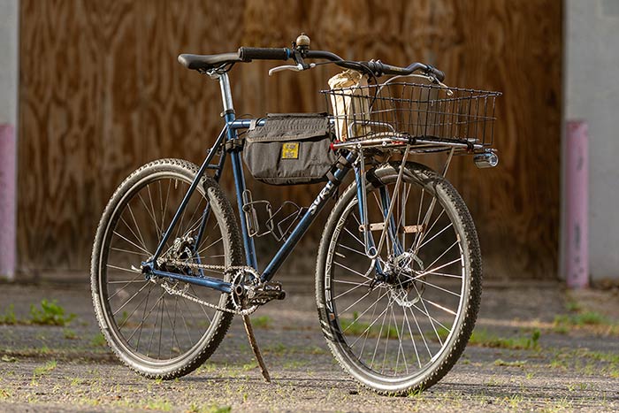 Blue Surly Straggler bike three-quarter front view built single speed with large front rack and basket and frame bag