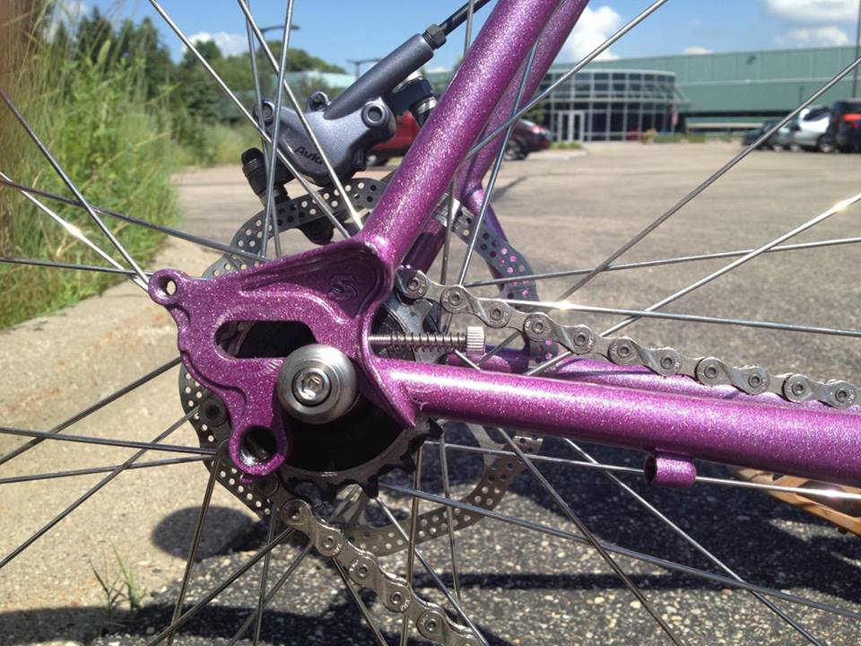 Right side dropout detail from a purple Surly Straggler bike, parked on a paved lot