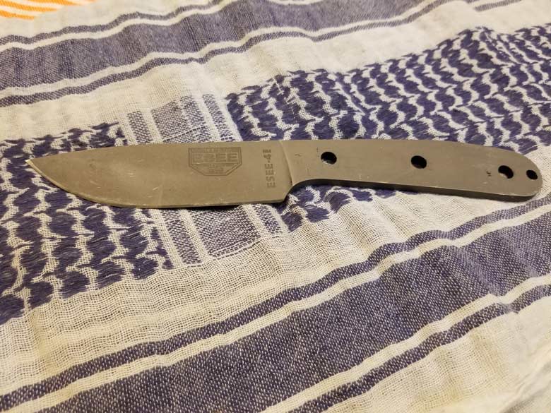Gray knife with ESEE logo and no handle covers laying on a woven towel