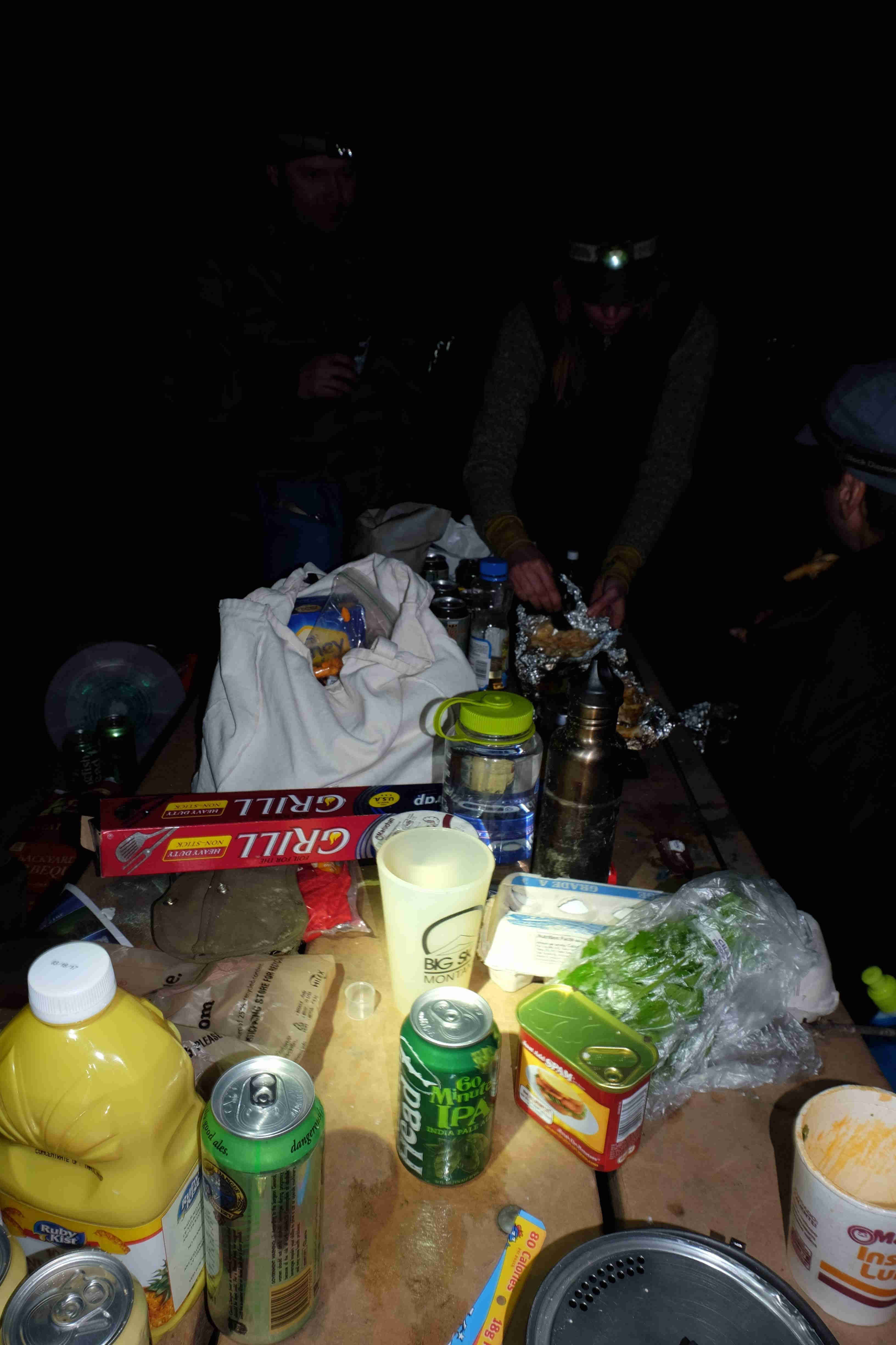 A picnic table covered in food and drink items, in the dark at night