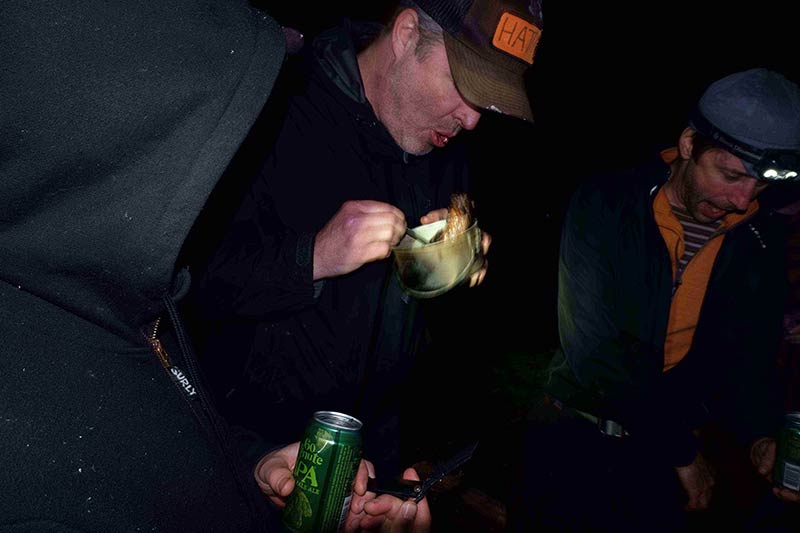 Front view of a person blowing on a cup of food, with 2 people sitting on each side, in the dark at night