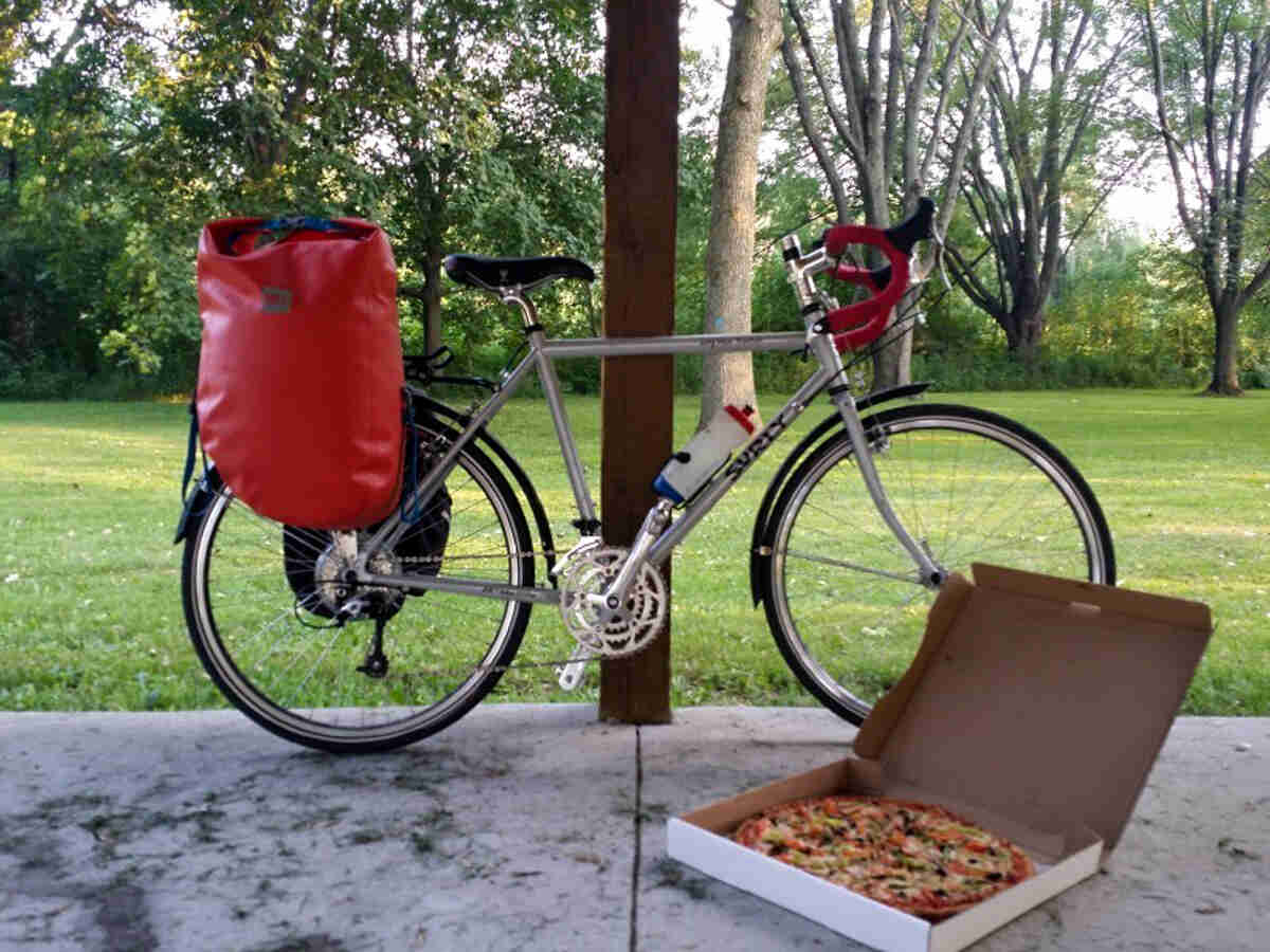 Right side view of a Surly Long Haul Trucker bike with a rear pack and a pizza on the ground next to the front wheel