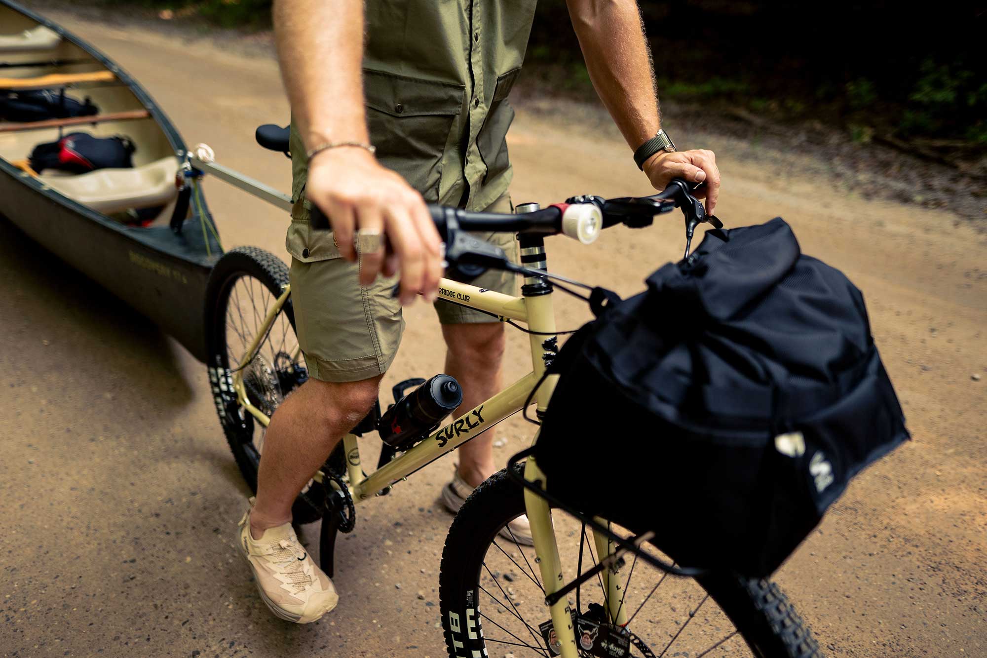 Cyclist standing over Surly Bridge Club bike with foot down on gravel road front rack with bag loaded and canoe in tow