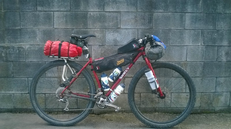 Right side view of a red Surly bike, loaded with gear, parked against a cinder block wall
