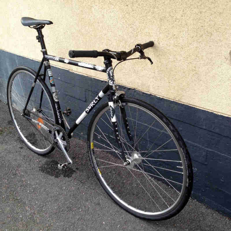 Right side view of a black Surly Steamroller bike, leaning against a stucco and brick wall