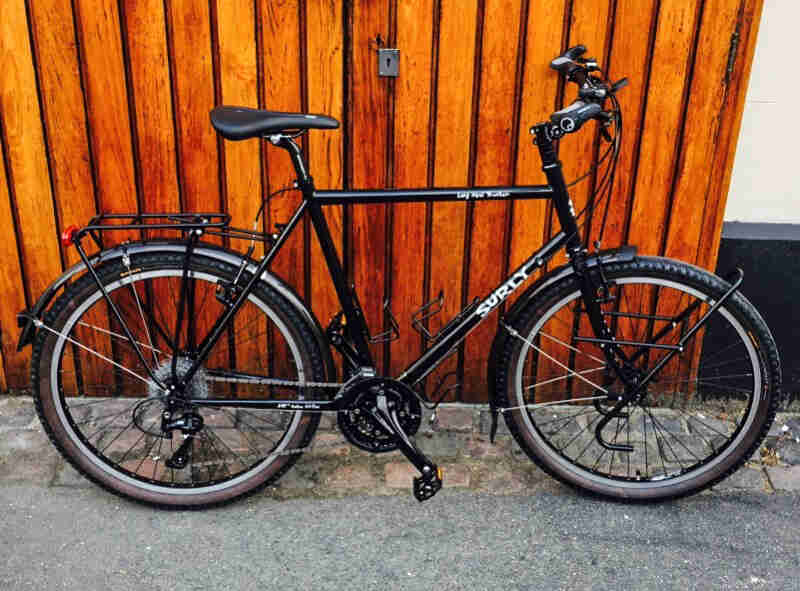 Right side view of a Surly Long Haul Trucker bike, black, leaning against a wood wall