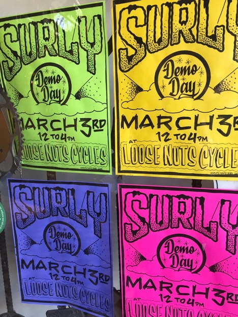 Four different colored Surly demo day fliers taped to a glass window 