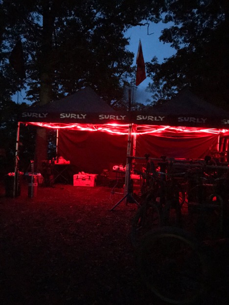 Two Surly pop up canopies with red string lights lit up in front at night in the woods