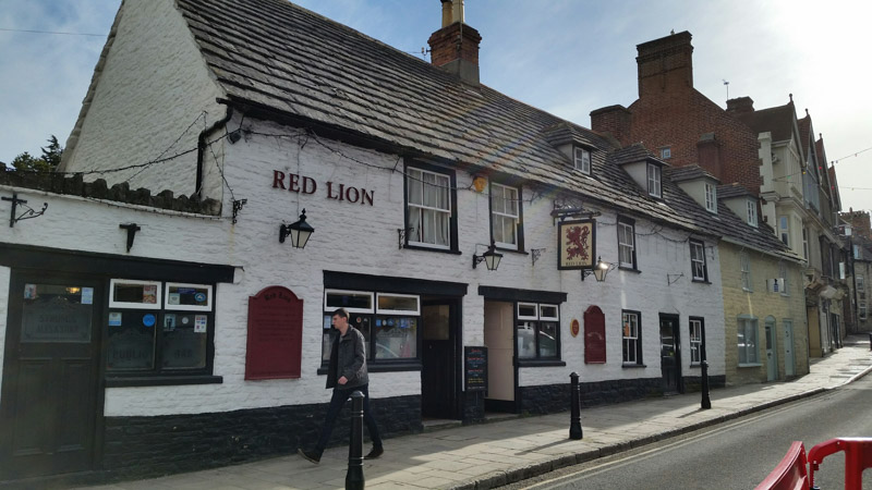 A person walking down a side walk in front of a building with the words, Red Lion, on it