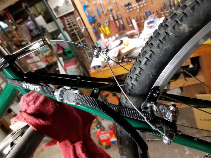 Zoom in view of a green Surly bike frame with a brake and cable on a rear wheel in a room with a workbench in background