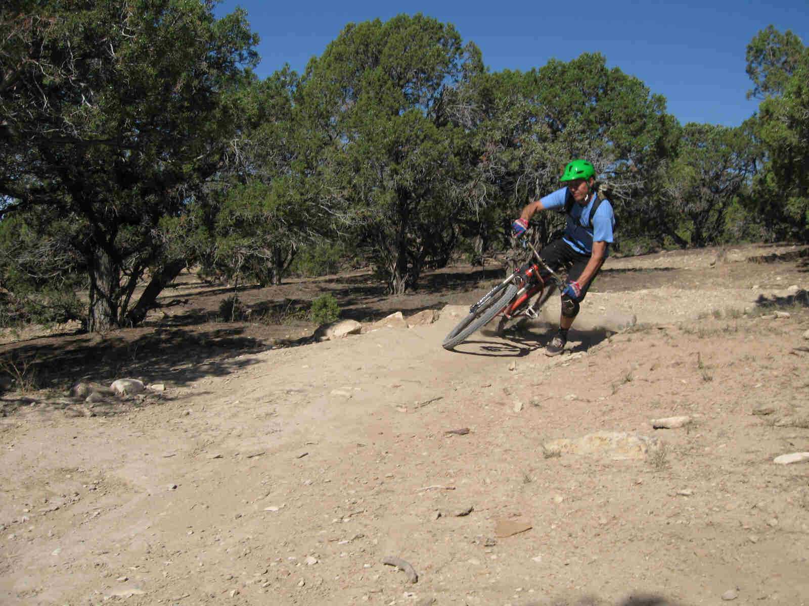 Front view of a cyclist riding a red Surly bike, rounding a turn on a rocky trail, with small trees behind them