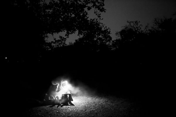 Black and white image of a person leaning over a campfire at night