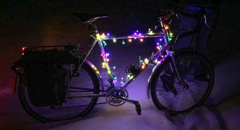 Right side view of a Surly bike, wrapped in christmas lights, standing in snow, at nighttime