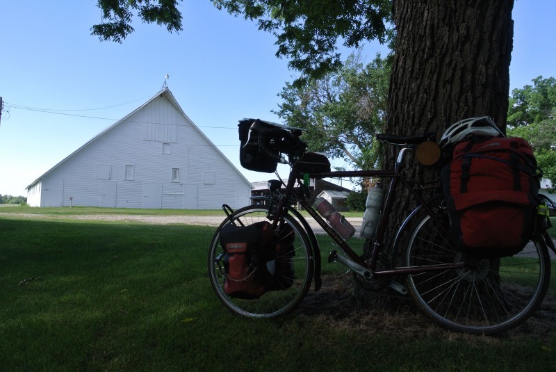 Left side view of a Surly Long Hauler Trucker bike loaded with gear, against a tree, with a white barn in the background