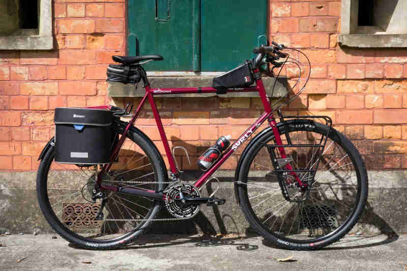 Right side view of a red Surly bike with a rear pack, parked on a sidewalk in front of a brick building 