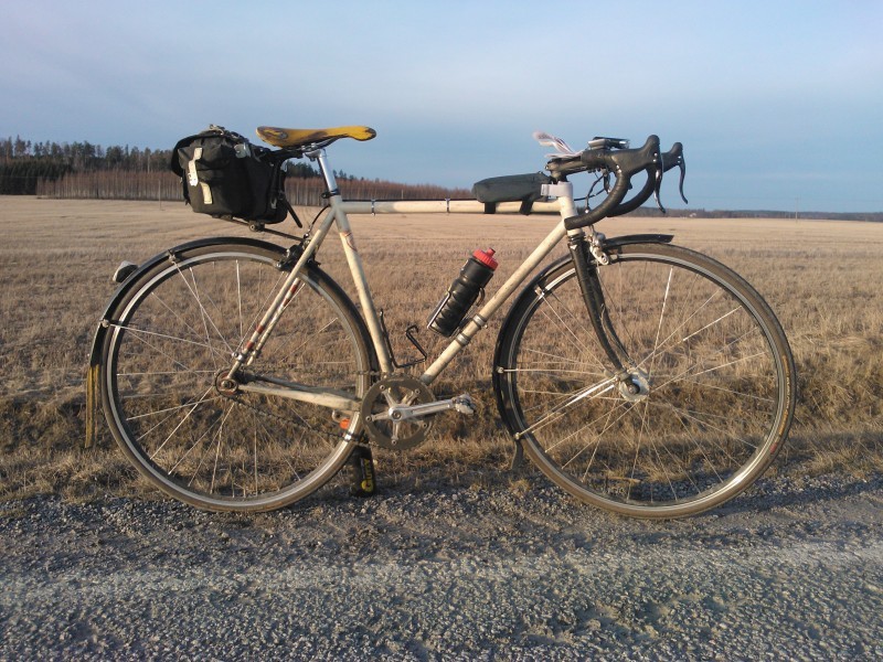 Right side view of a tan Surly bike with a seat pack and water bottle, standing next to a field of brown grass
