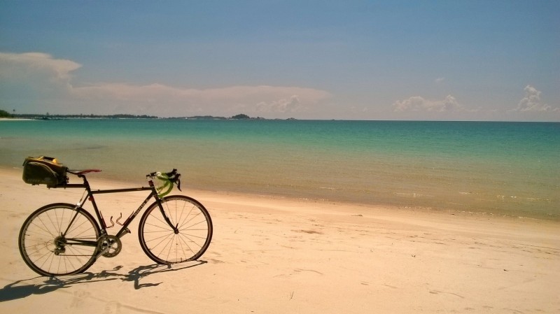 Right side view of a Surly bike, on a sandy beach, facing turquoise waters