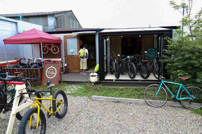 Outside, storefront view of the Wakka bicycle life shop, with Surly bikes parked all around, and a person in the doorway